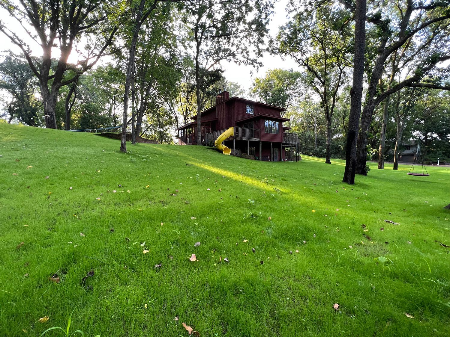 A large house is sitting on top of a lush green hill surrounded by trees