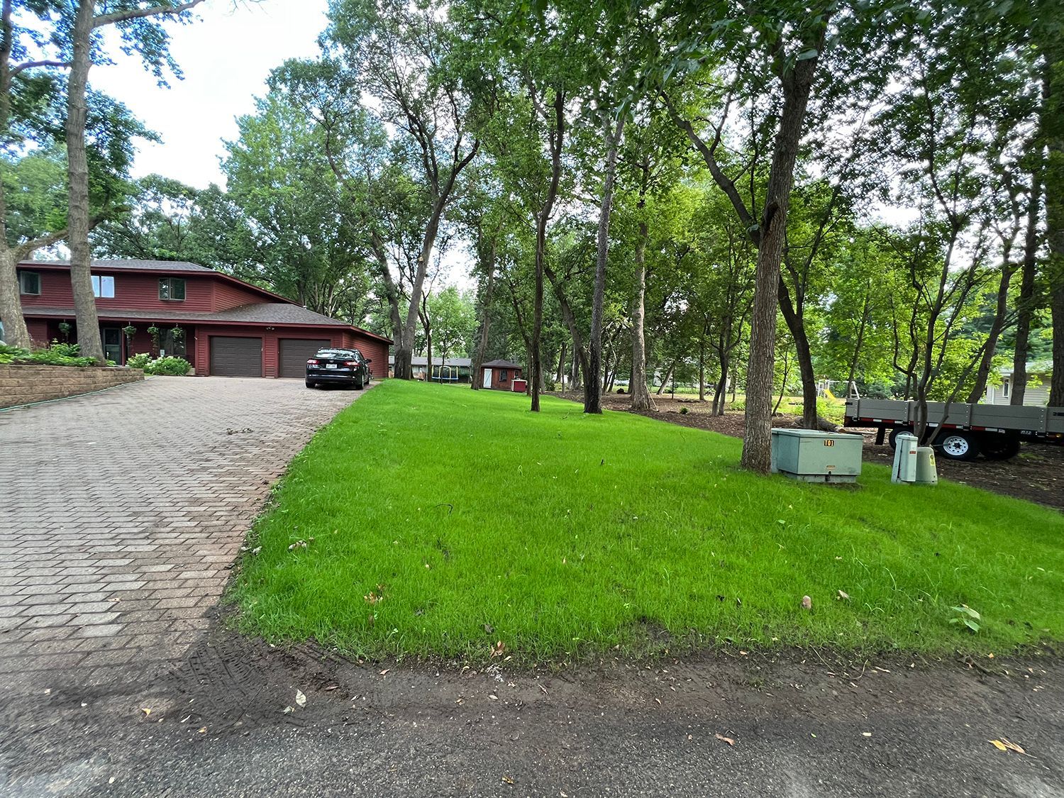 A car is parked in the driveway of a house surrounded by trees