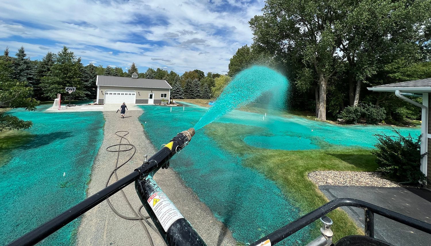 A person is spraying green fertilizer on a lawn
