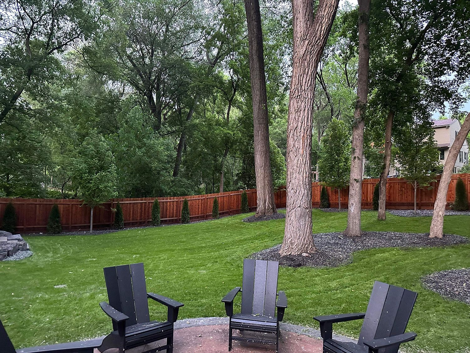A group of chairs are sitting on a patio in a backyard surrounded by trees
