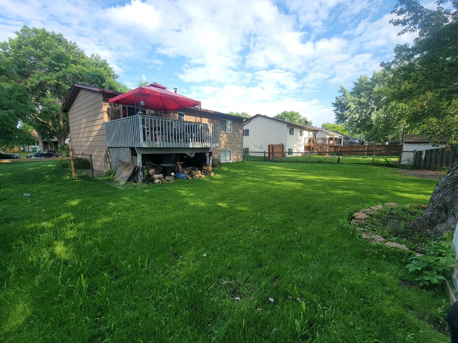 The backyard of a house with a large deck and a red umbrella