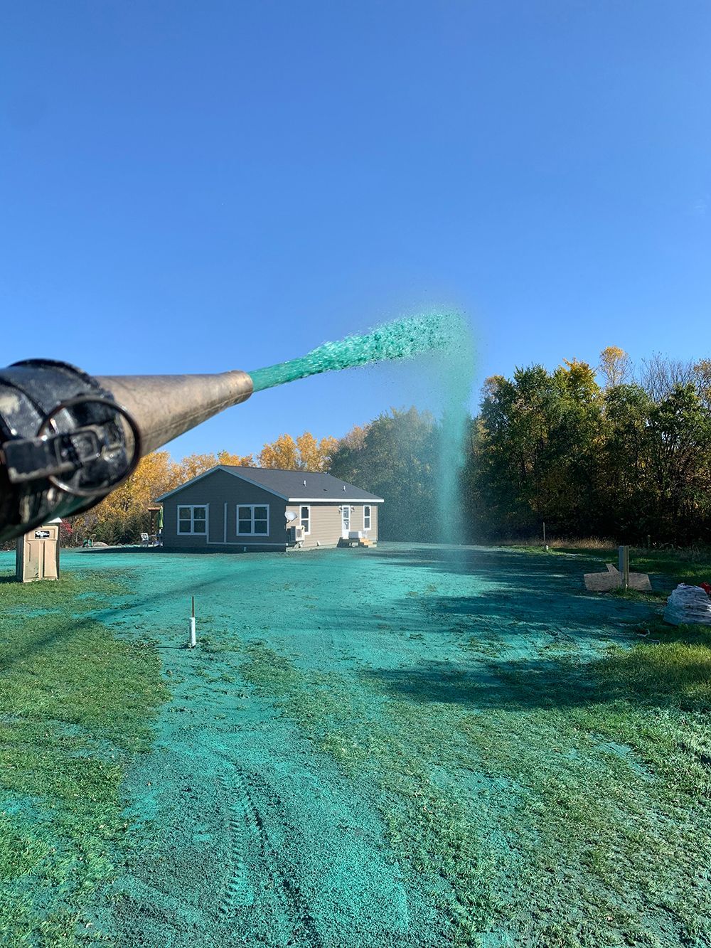 A person is spraying green fertilizer on a lawn in front of a house