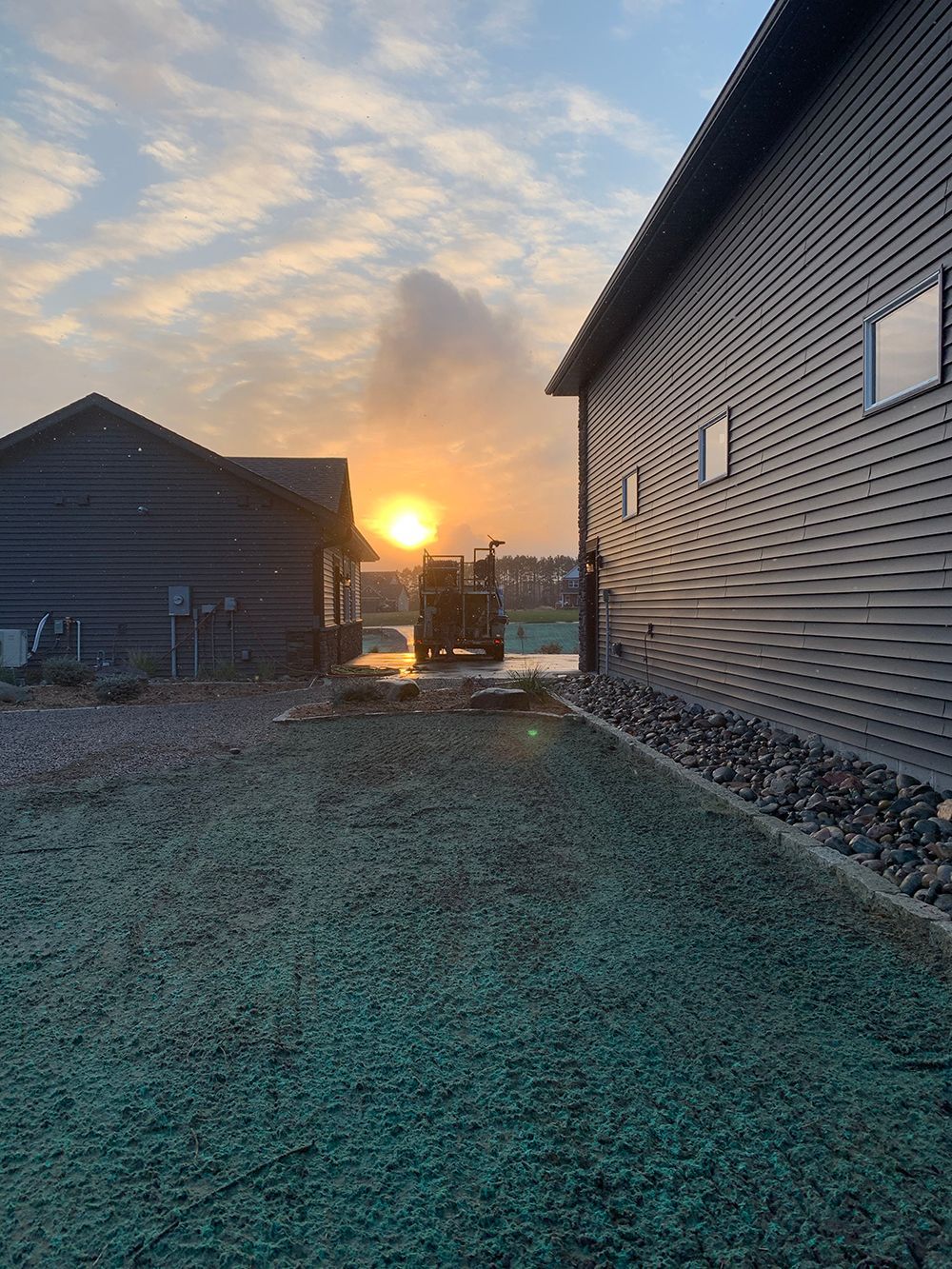 The sun is setting behind two houses in a backyard