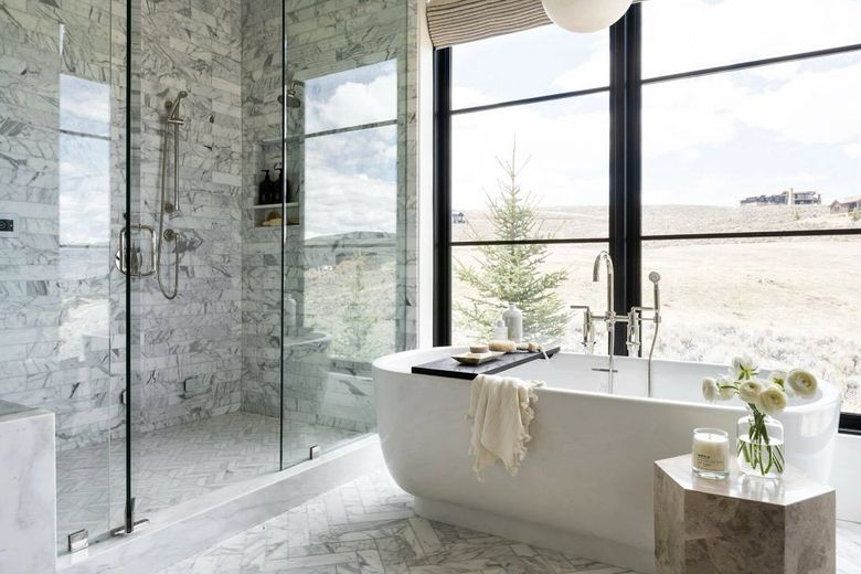 Luxurious bathroom with a freestanding tub, glass shower, and large window overlooking a landscape.