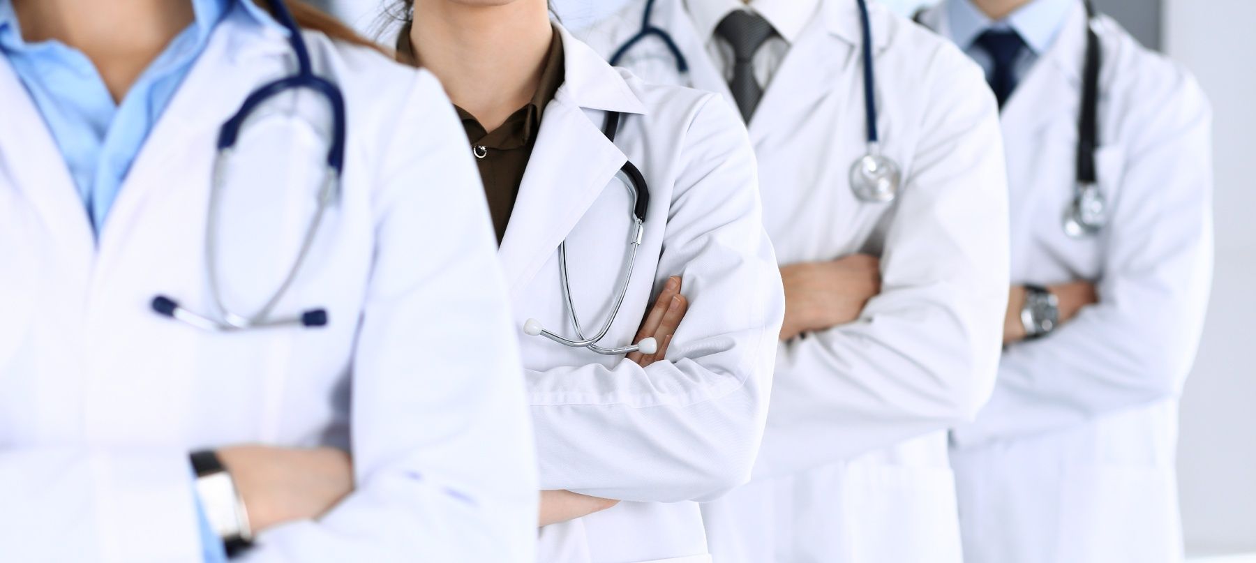 Group of doctors standing together, arms crossed, wearing white coats, stethoscopes.