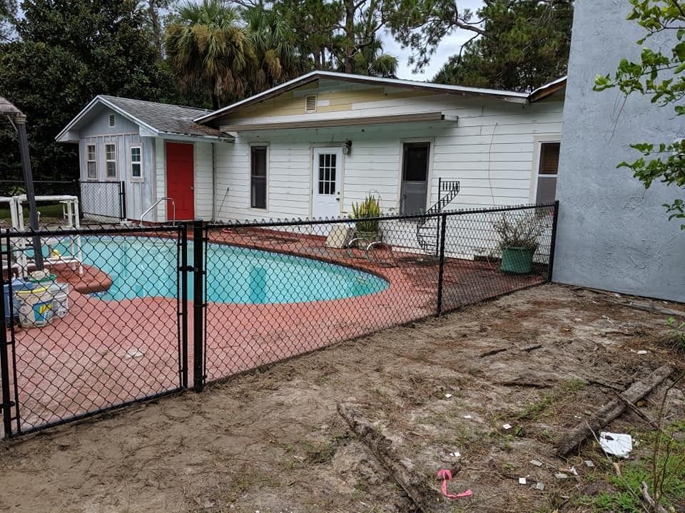 Pool area with a black fence, white house, and red door.