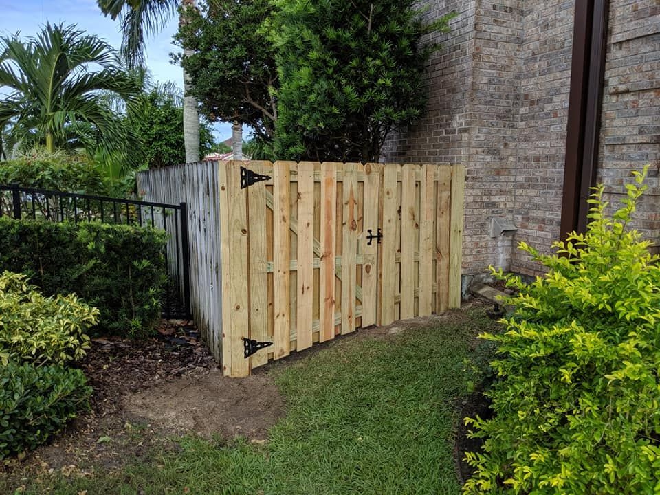 Wooden fence and gate against a brick wall, with landscaping and green grass.