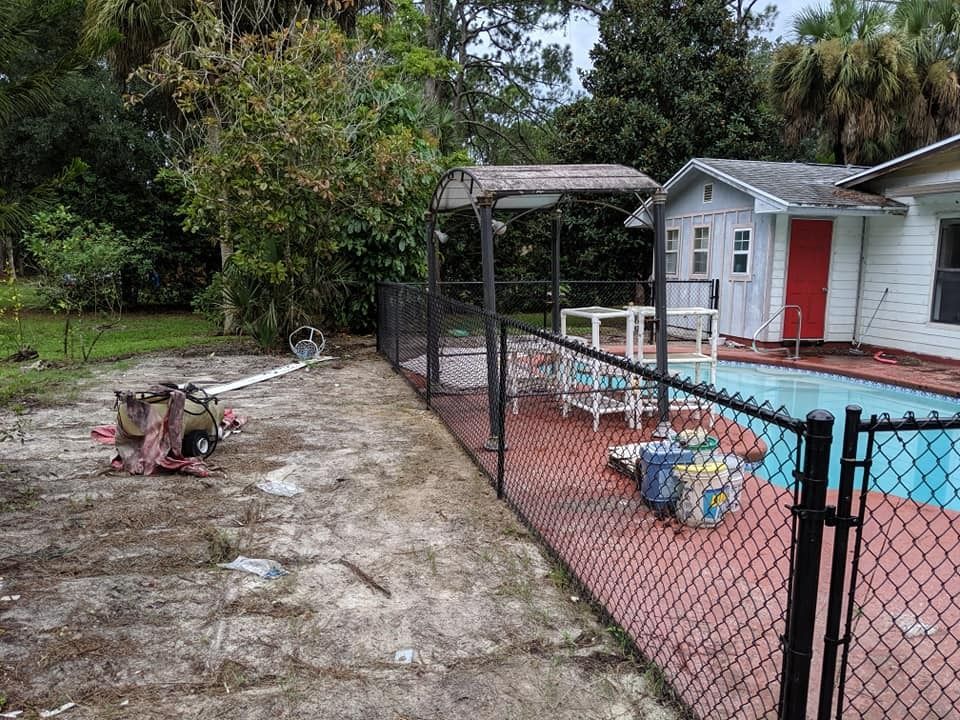 Backyard with chain-link fence, pool, small white house, lounge chairs, and pool cleaning equipment.