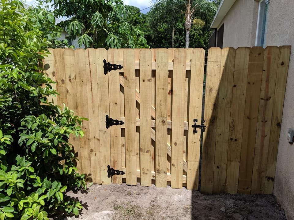 Wooden gate in a backyard, with black hinges and latch.