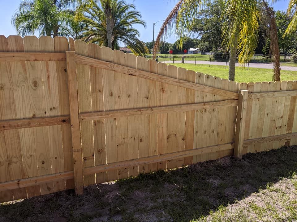 Wooden fence with a gate, in a sunny outdoor setting with palm trees.