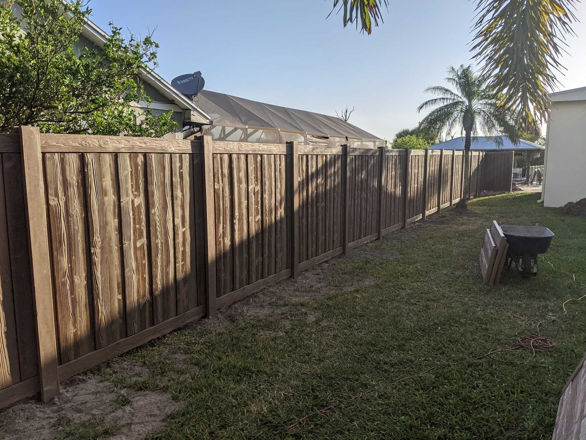 Wooden fence in a backyard with patchy grass. A wheelbarrow sits nearby.