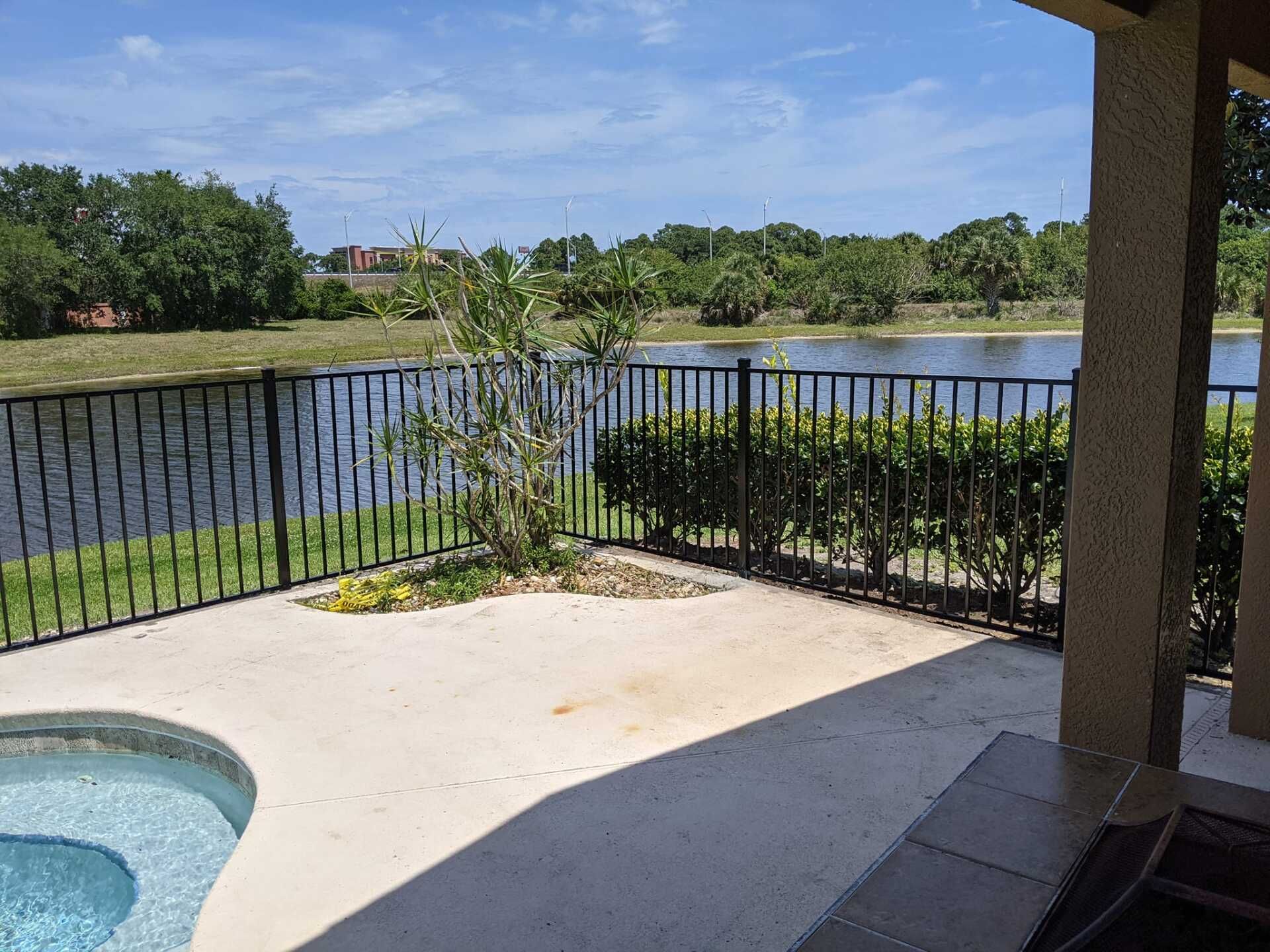 Patio overlooking a lake, with black fence. Sunny day, with trees and blue sky.