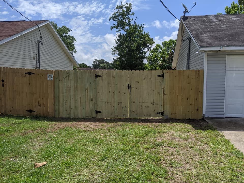 Wooden fence with gate, between two houses, against a partly cloudy sky.