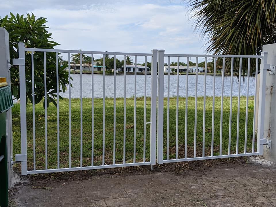 White metal gate, open, overlooking water with houses in the background.