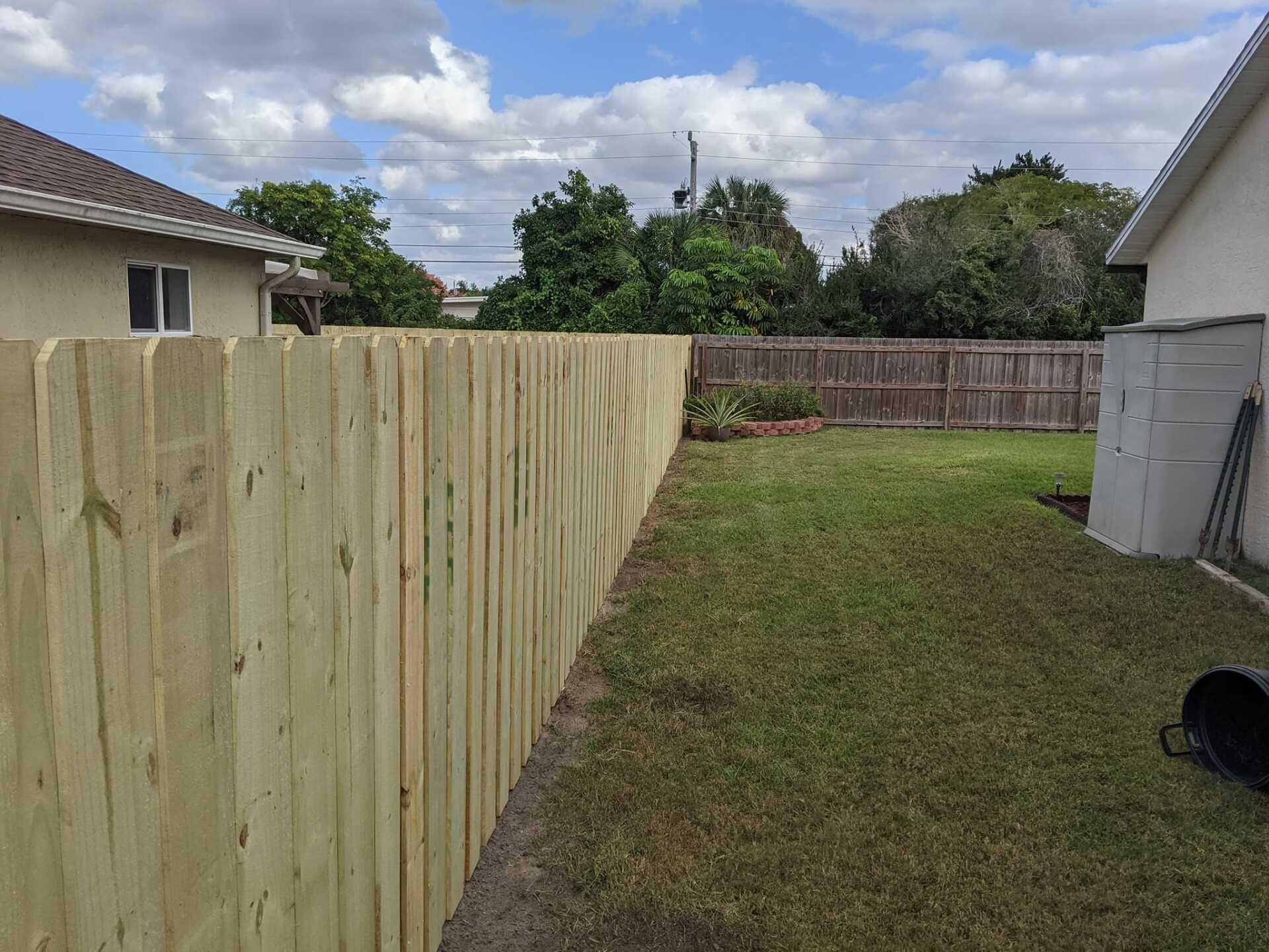Wooden fence bordering a backyard with green grass, a shed, and a neighboring brown fence.