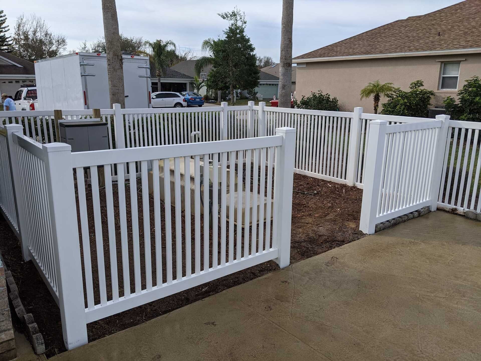 White picket fence encloses a small yard with mulch, visible from a concrete patio.