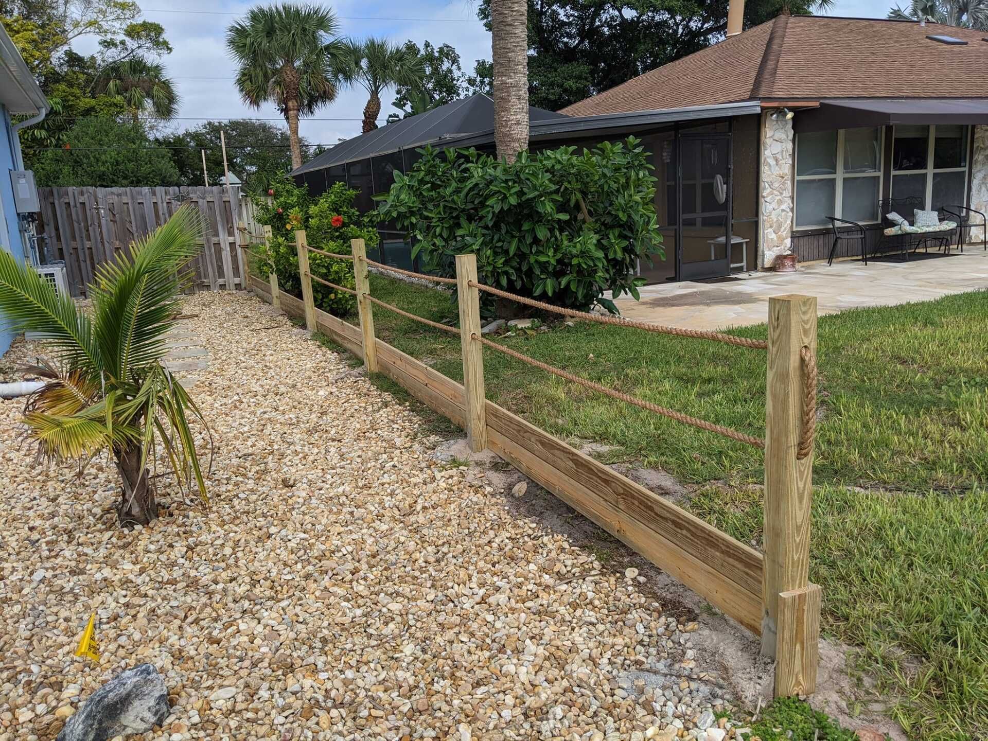 Wooden fence with rope between posts in a yard with gravel and grass.