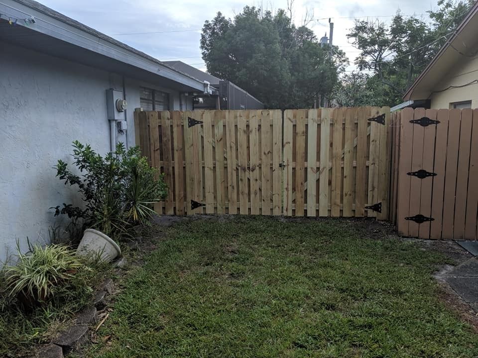 Wooden fence in backyard, connecting to a house and another building. Green grass in front.
