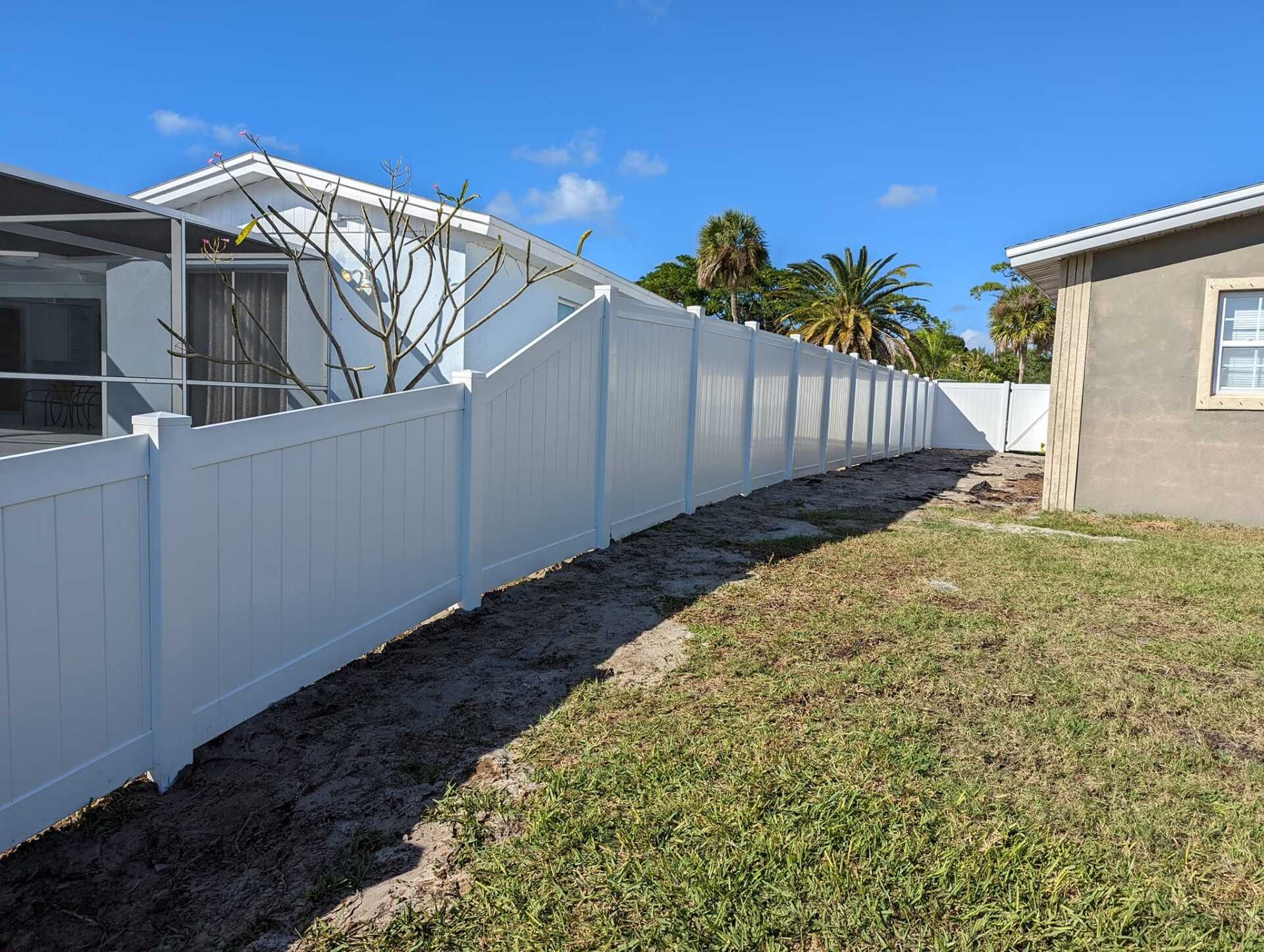 White vinyl fence along grassy yard, sunny day, houses in background.