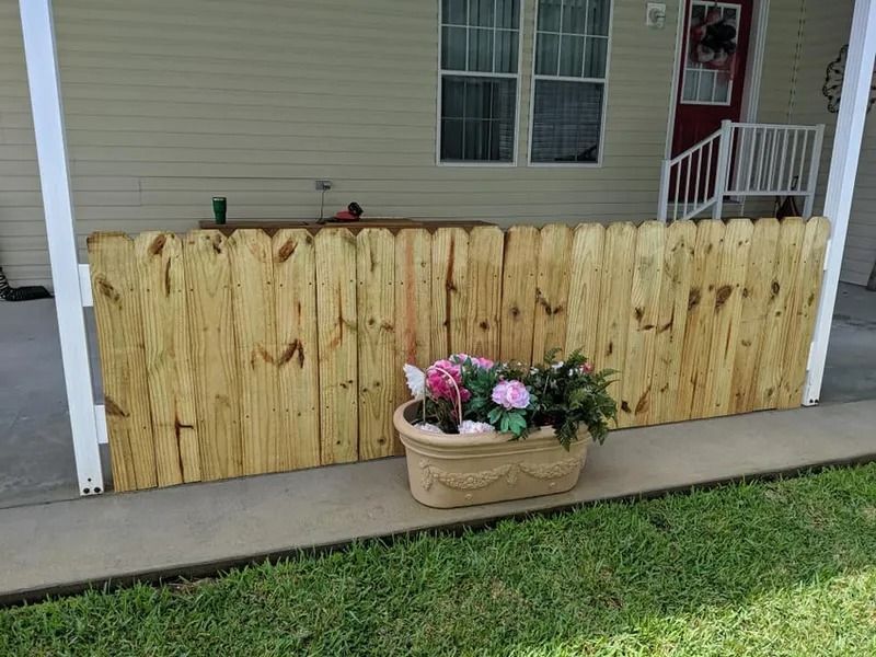 Wooden fence with flower pot on a porch. Green grass and house exterior in background.