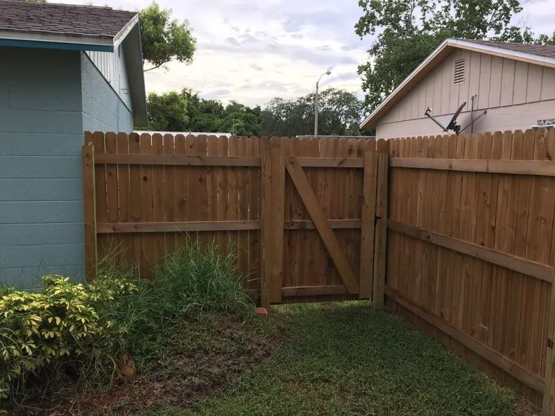 Wooden fence with a gate in a grassy yard, between two houses.