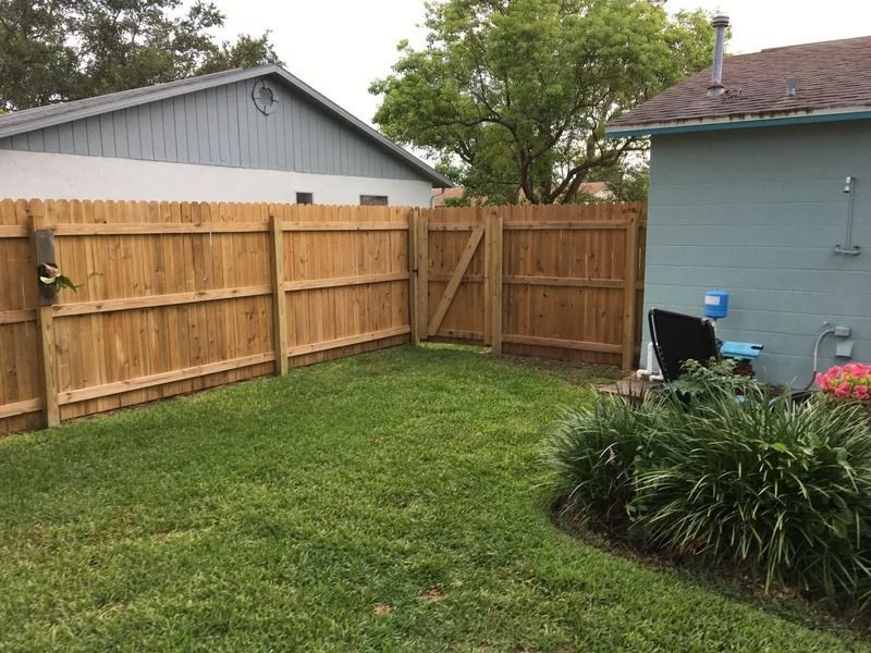 Wooden fence with gate in grassy backyard, next to a blue house and a light-colored house.