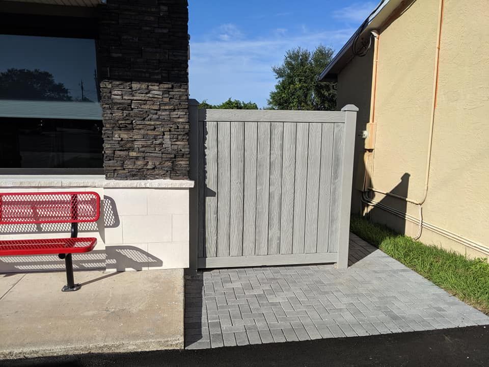 Gray wooden gate on brick patio next to a building with stone and red bench.