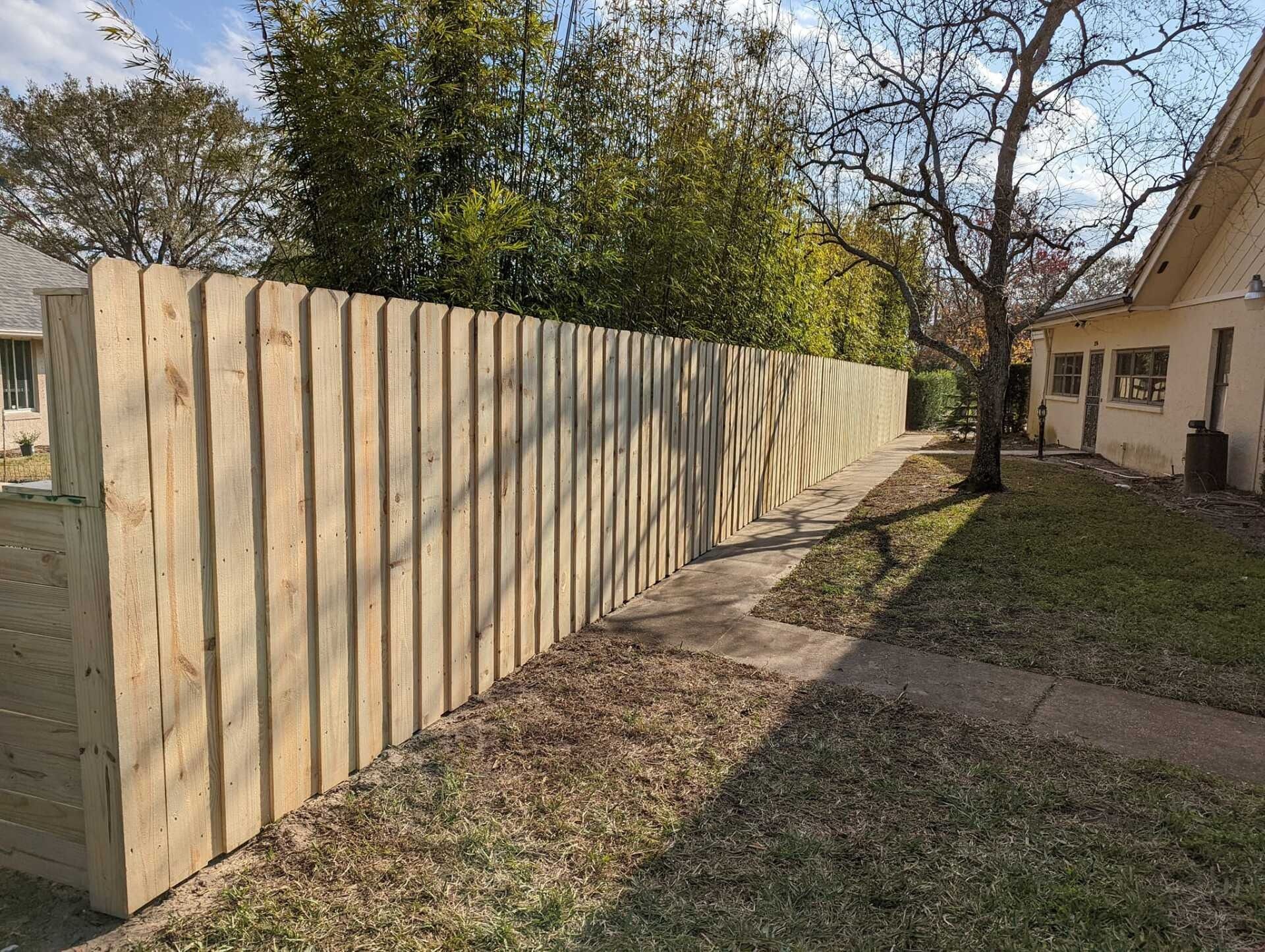 Wooden fence along a grassy yard, beside a house with a sidewalk.