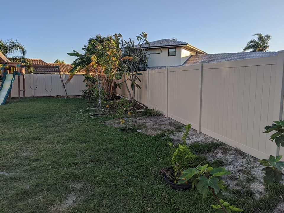 Backyard with a tan fence, grass, trees, and a house in the background. Playground on the left.