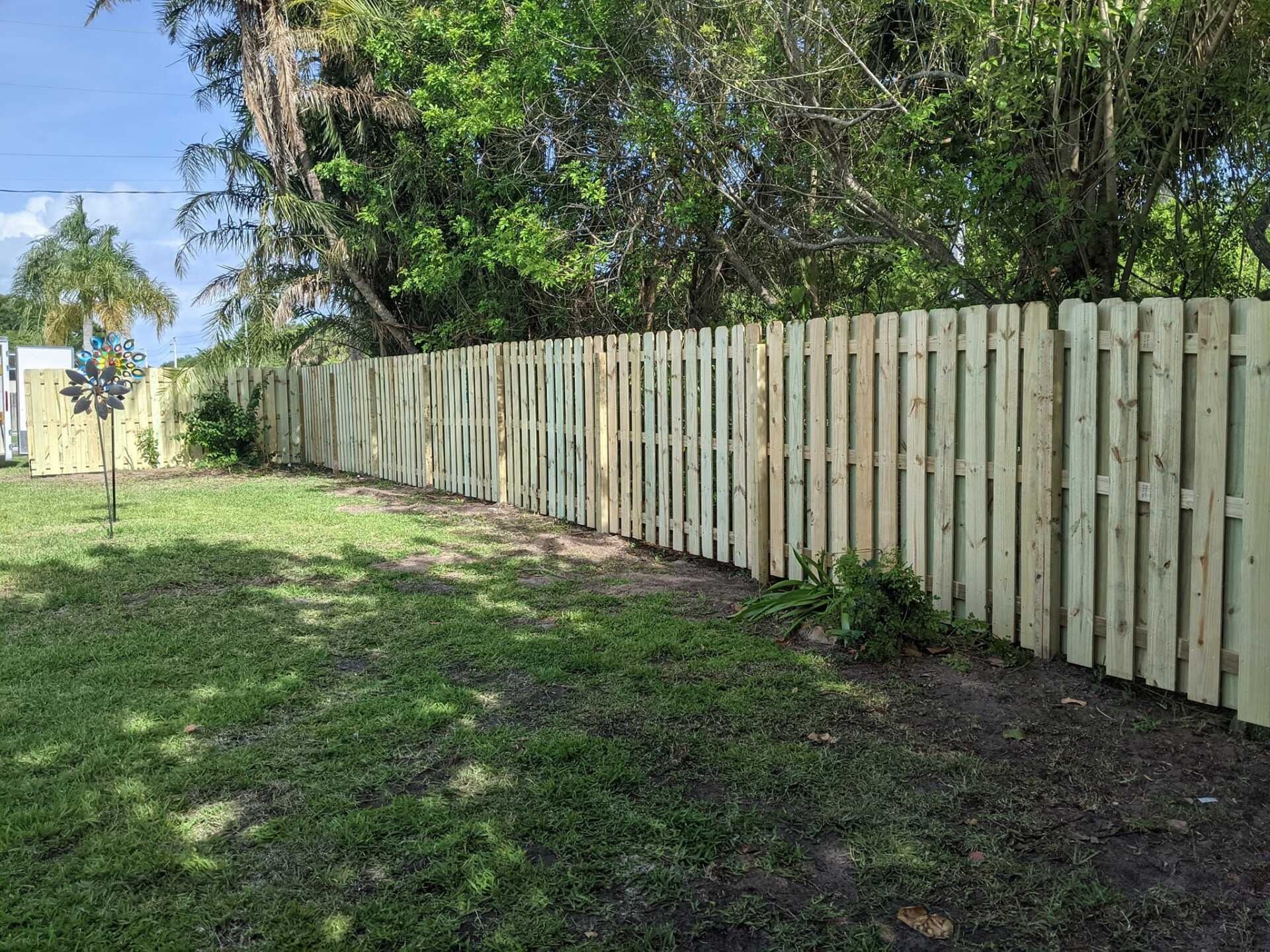 A wooden fence encloses a backyard with green grass and trees.