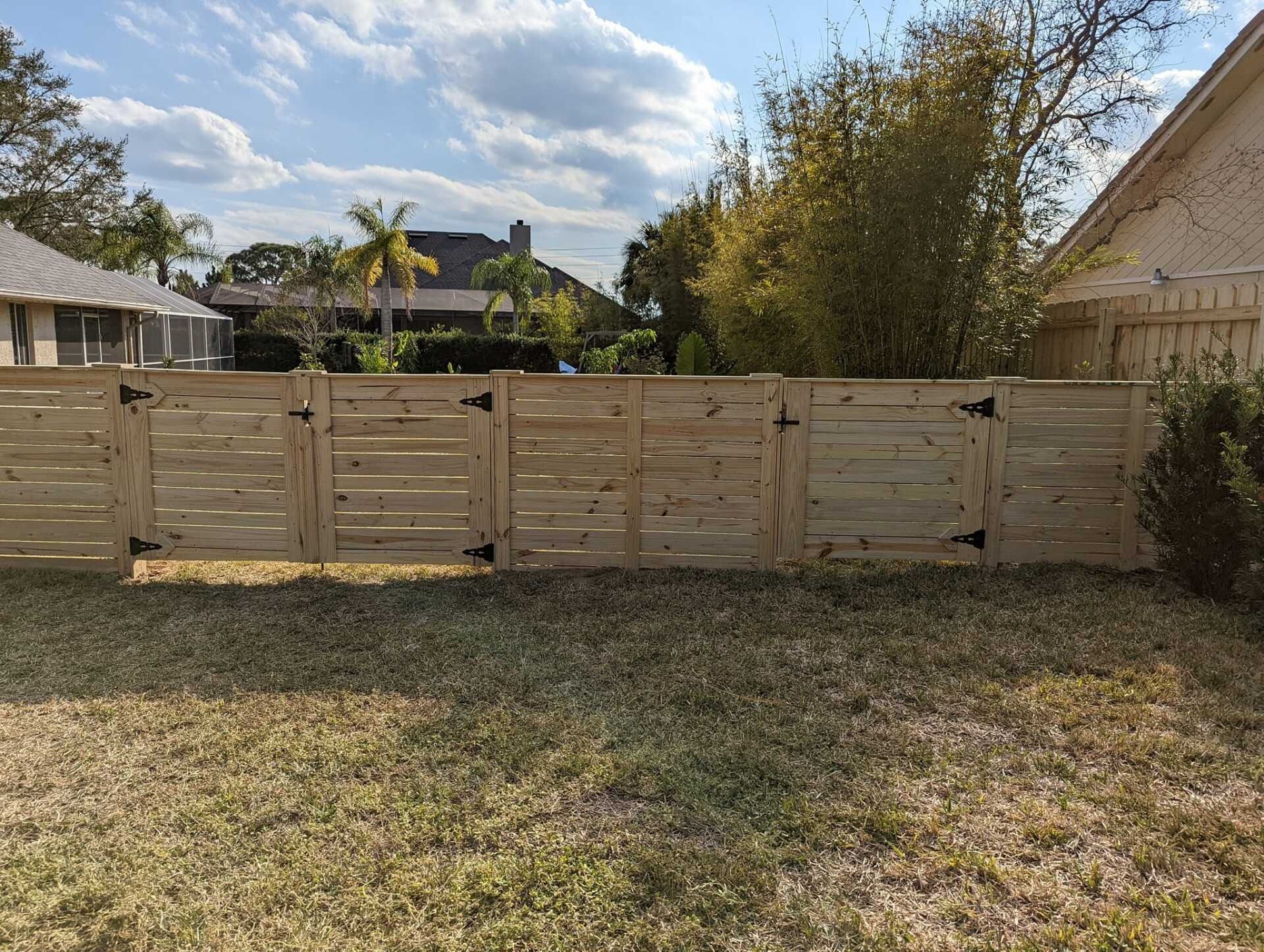 Wooden fence with three gates in a backyard, under a partly cloudy sky.