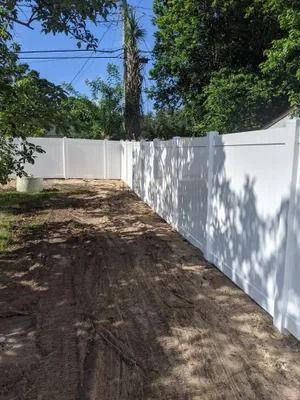 White vinyl fence along a dirt path, trees in background, sunny day.