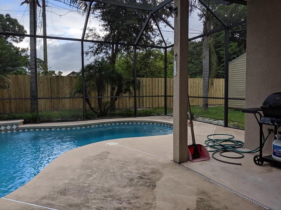 Pool area with a screened enclosure. Pool, patio, grill, and fence visible. Overcast sky.