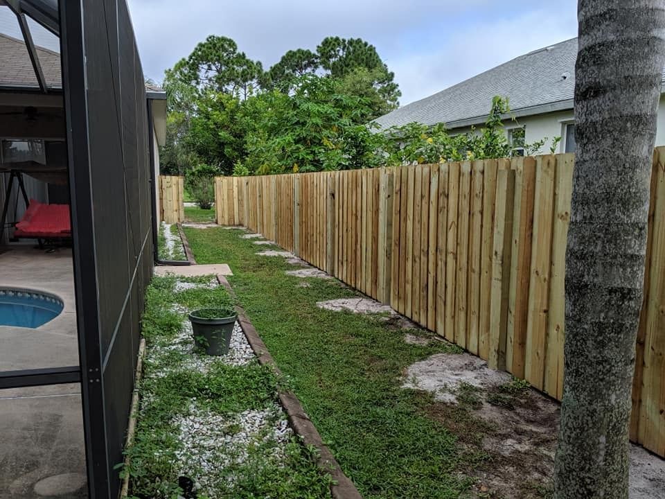 Backyard view: wooden fence bordering a grassy area with stepping stones. A screened-in patio and pool are to the left.