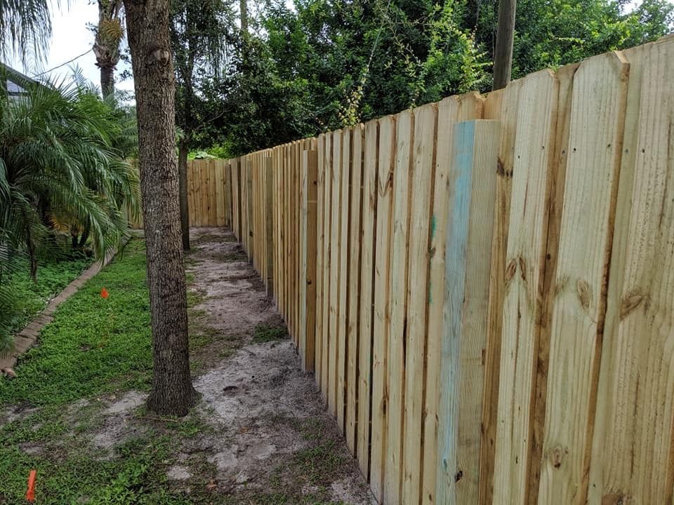 Wooden fence with vertical planks in a backyard setting, trees and grass visible.