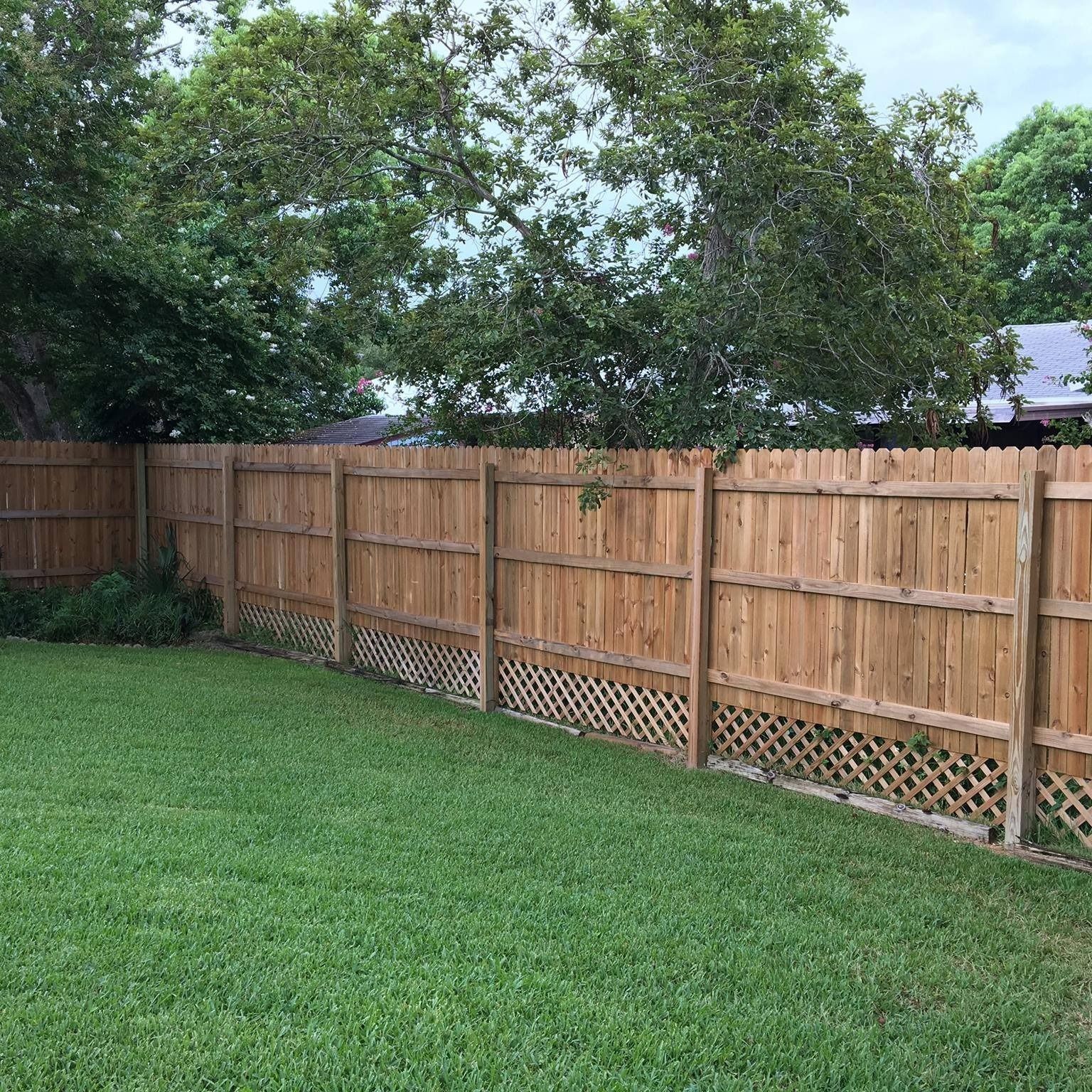 Wooden fence bordering green lawn, trees in background, overcast day.