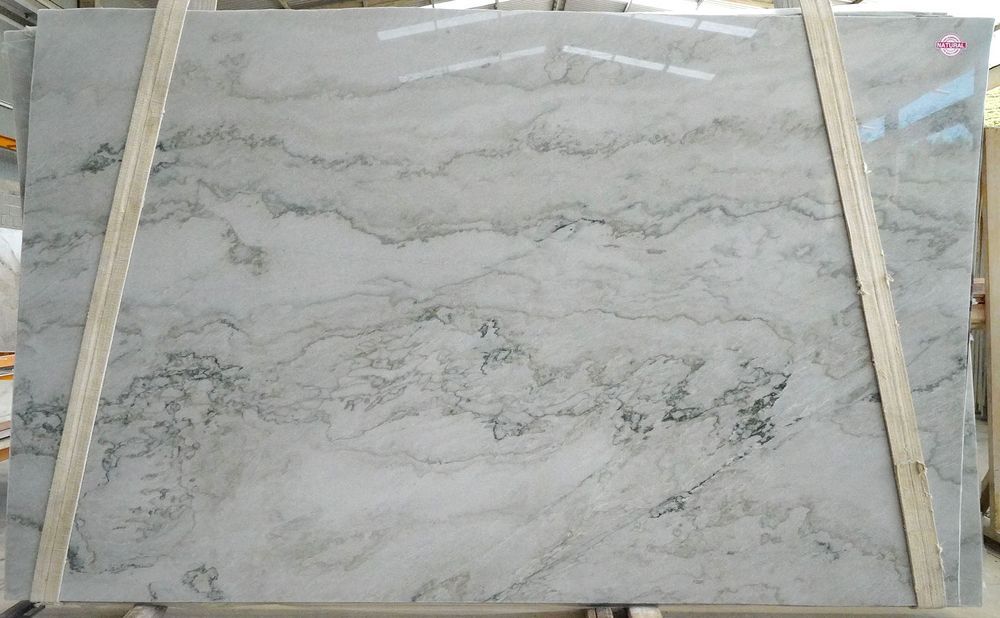 Large light gray marble slab with subtle wavy dark veining, framed by wooden supports in a storage area