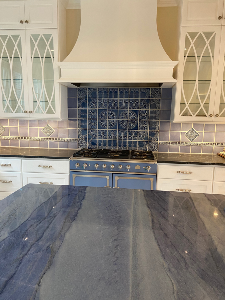 Kitchen with blue and white cabinets, range, and countertop. Blue patterned backsplash.