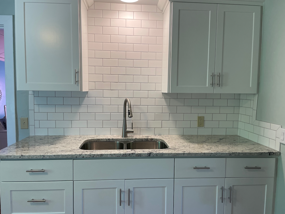 White kitchen with granite countertops, subway tile backsplash, and stainless steel sink.