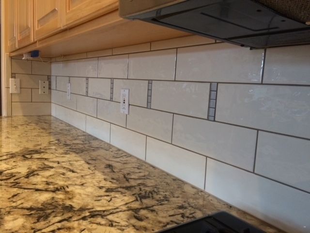White tiled kitchen backsplash with granite countertop and wooden cabinets.