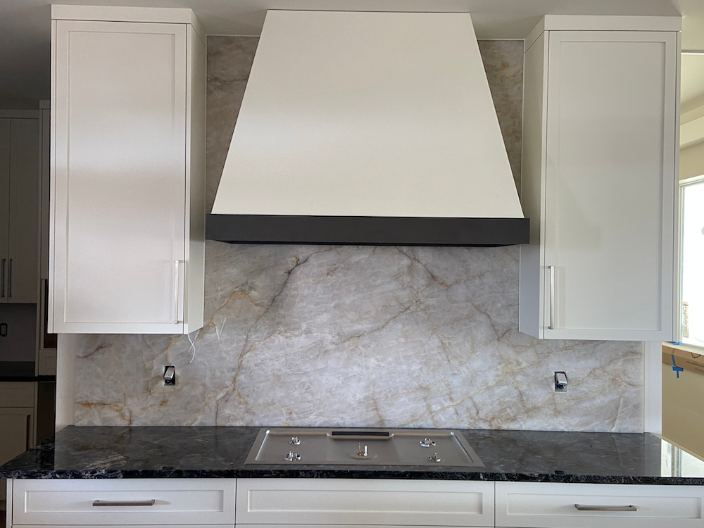 Kitchen with white cabinets, range hood, and marble-look backsplash over a stovetop.