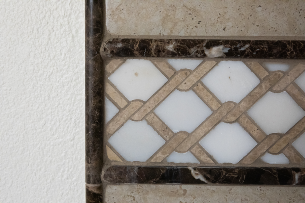 Decorative tile border with interwoven tan and white pattern, framed by brown and beige stone.