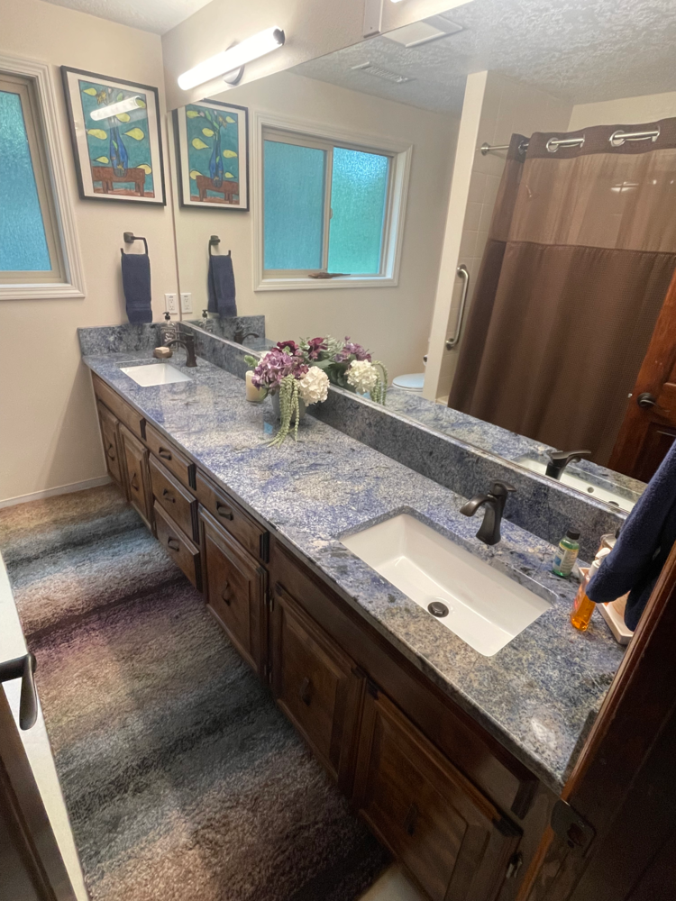 Bathroom with blue granite countertop, two sinks, brown cabinets, and a long mirror.
