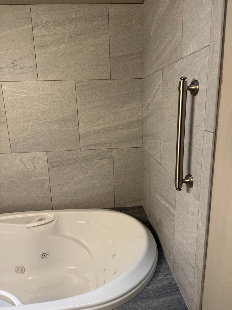 Jacuzzi with grab bar on tiled wall.
