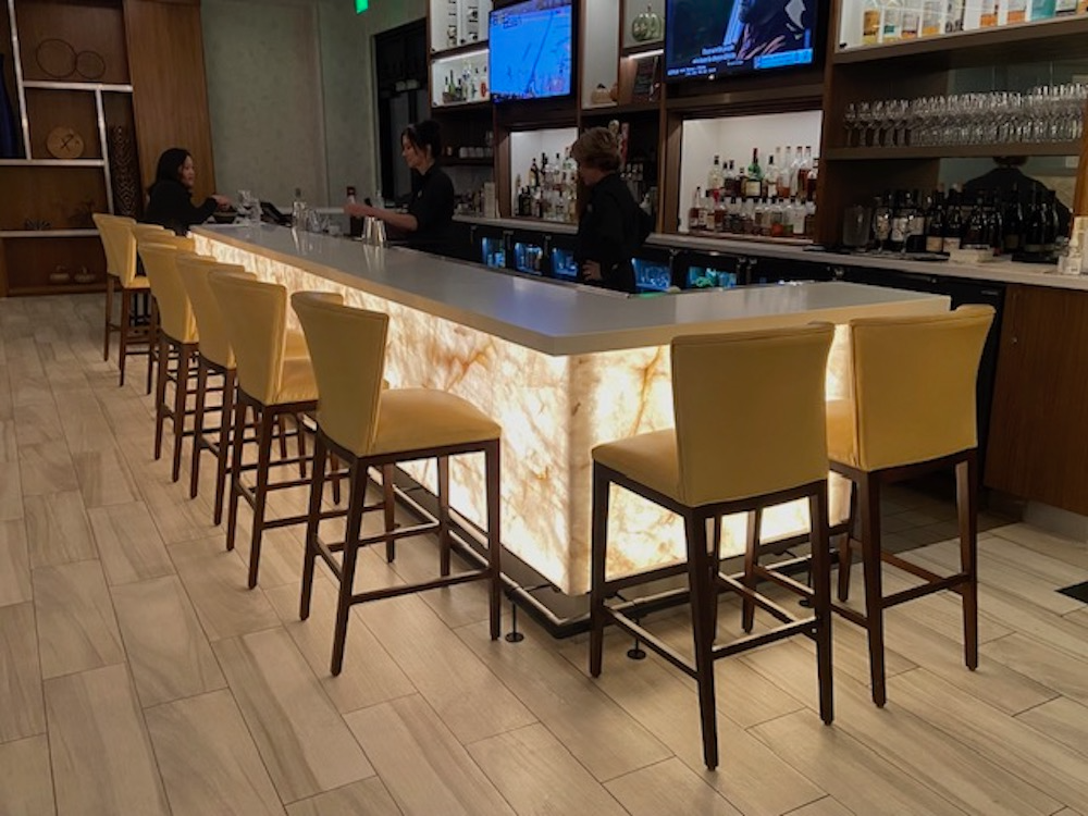 Bar with illuminated front, yellow stools, bartenders, and drinks.