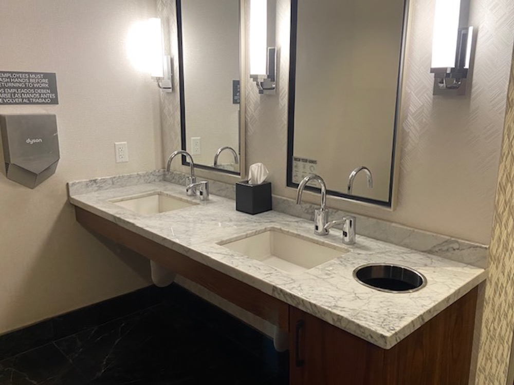 Public restroom with two sinks, mirrors, and a wastebasket on a granite countertop.