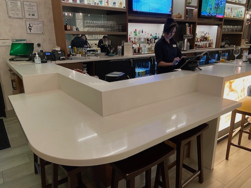 Bar with white countertop, brown stools, and a bartender working behind the bar.