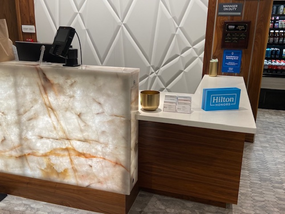 Hotel front desk with a lit stone facade and white geometric wall.