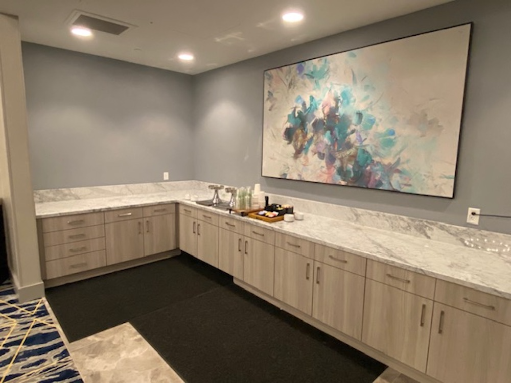 A room with a countertop, cabinets, and a large abstract painting.