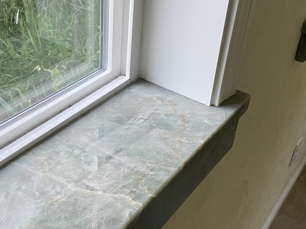 Green marble windowsill next to a white window frame and wall.